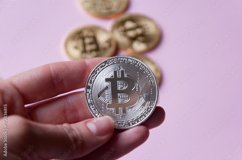 The hand holds a silver coin bitcoin on a pinkbackground. In the background there are several gold coins bitcoin. Concept of crypto currencies. The hand holds a silver coin bitcoin on a pinkbackground. In the background there are several gold coins bitcoin. Concept of crypto currencies.