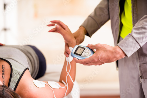 Close-up of a deportist holding with one hand the electric machine and putting the electrostimulator electrodes the arm of a female deportist photo