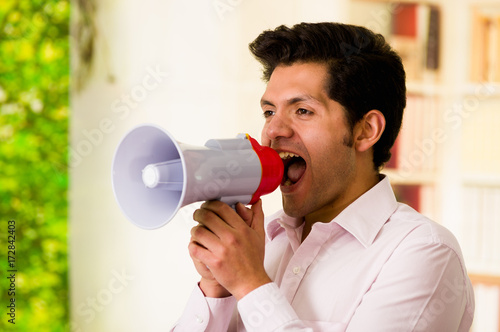 Close up of ayoung man shouting with a megaphone, close to his mouth in a blurred background photo