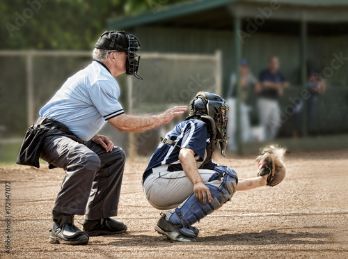 Foto Umpire and catcher, just as ball hits catcher's mitt, dugout and players in back