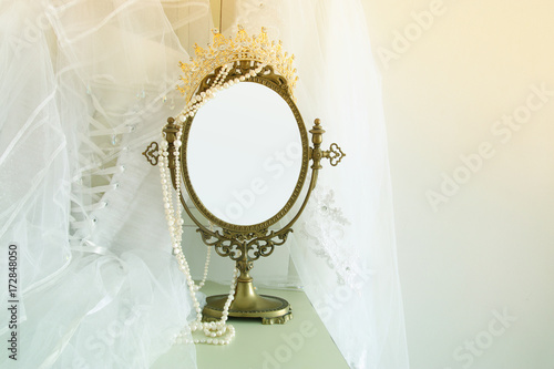 Old vintage oval mirror and beautiful white wedding dress and veil on chair. Copy space for mock up, montage or design layout