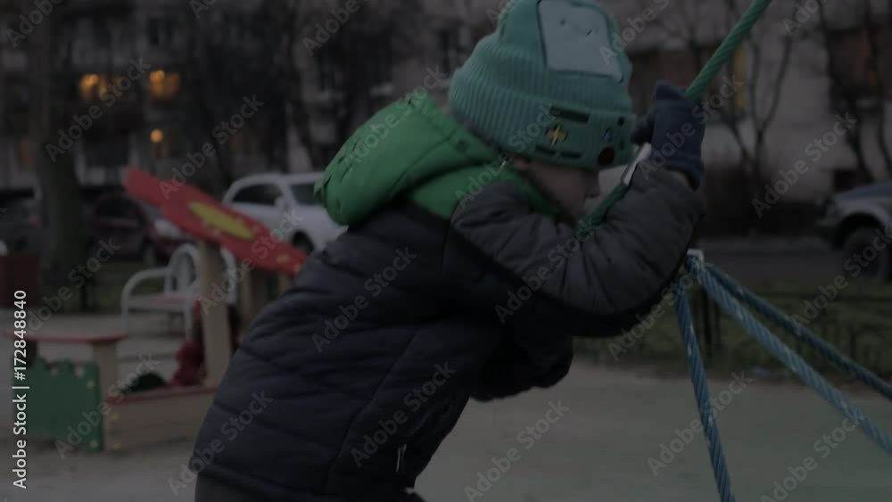 Kid having fun on the playground during his evening walk. Boy climbing web and getting down holding the rope Kid having fun on the playground during his evening walk. Boy climbing web and getting down holding the rope