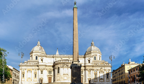 Obelisk of the Plaza called the Esquiline and facade of the papal Basilica called Santa Maria Maggiore, without people in sight and with a blue sky with very light clouds. In Rome, Italy photo