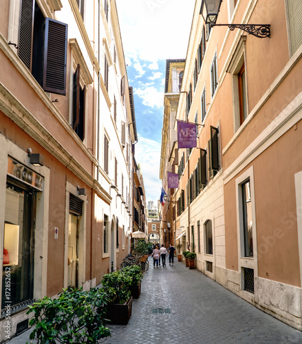 Fototapeta Naklejka Na Ścianę i Meble -  Typical narrow cobbled shopping street of Rome, Italy. With people walking and a blue sky with clouds