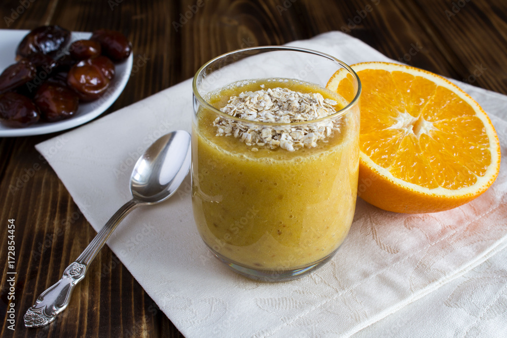 Healthy breakfast: smoothie from orange, dates and oat flakes on the wooden background Healthy breakfast: smoothie from orange, dates and oat flakes on the wooden background