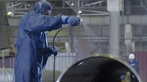 Male holding spray gun and painted steel. Man paints pipe atomizer