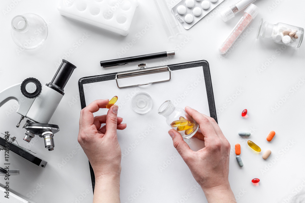 Obraz premium Do medcal tests. Hands hold pills near microscope on white background top view