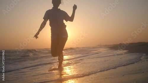 A joyous slender girl runs along the waves in splashes of water at sunset. HD, 1920x1080. slow motion.
