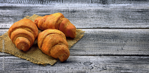 Fresh croissants on an old wooden table in a rural setting.