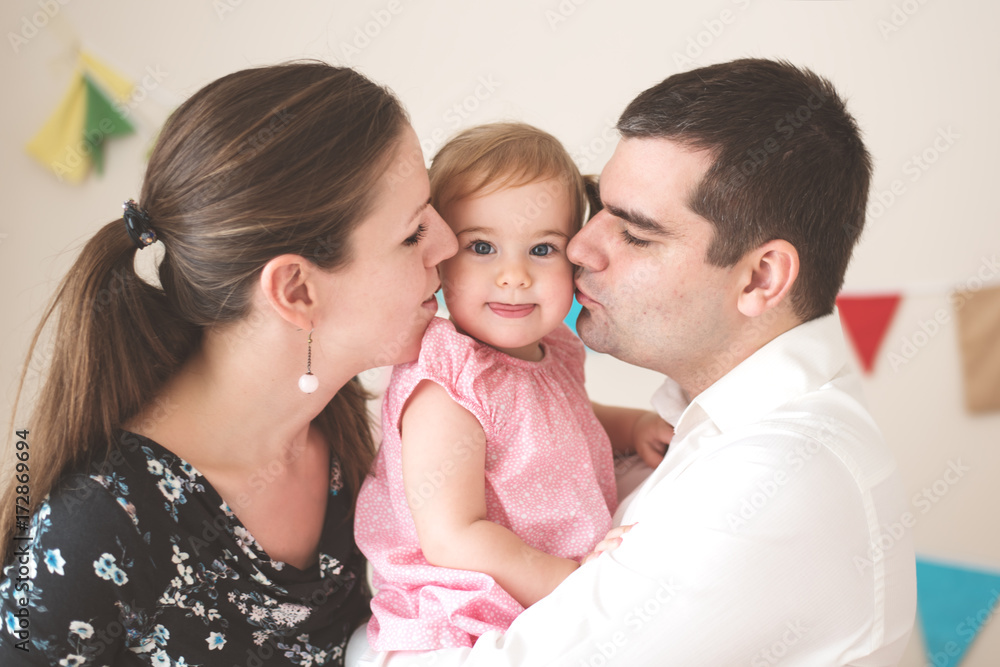 Mother and father snuggling with their little girl and kissing her Mother and father snuggling with their little girl and kissing her