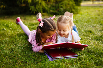 Two young girls lying on the grass outdoors reading separate books. These siblings are enjoying time together as family during summer