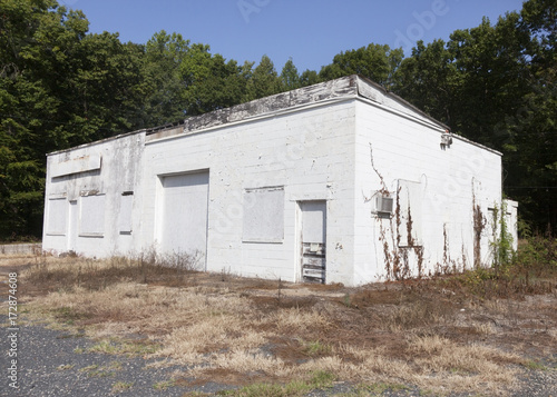 Abandoned, shuttered gas station grocery store with trees and blue sky.