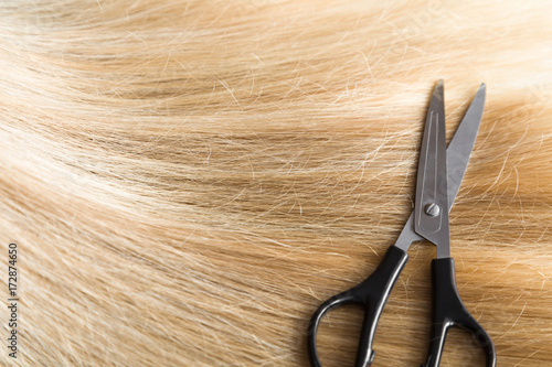 Scissors on the blonde hair background. Cares about a healthy and clean hair. Beauty salon. 