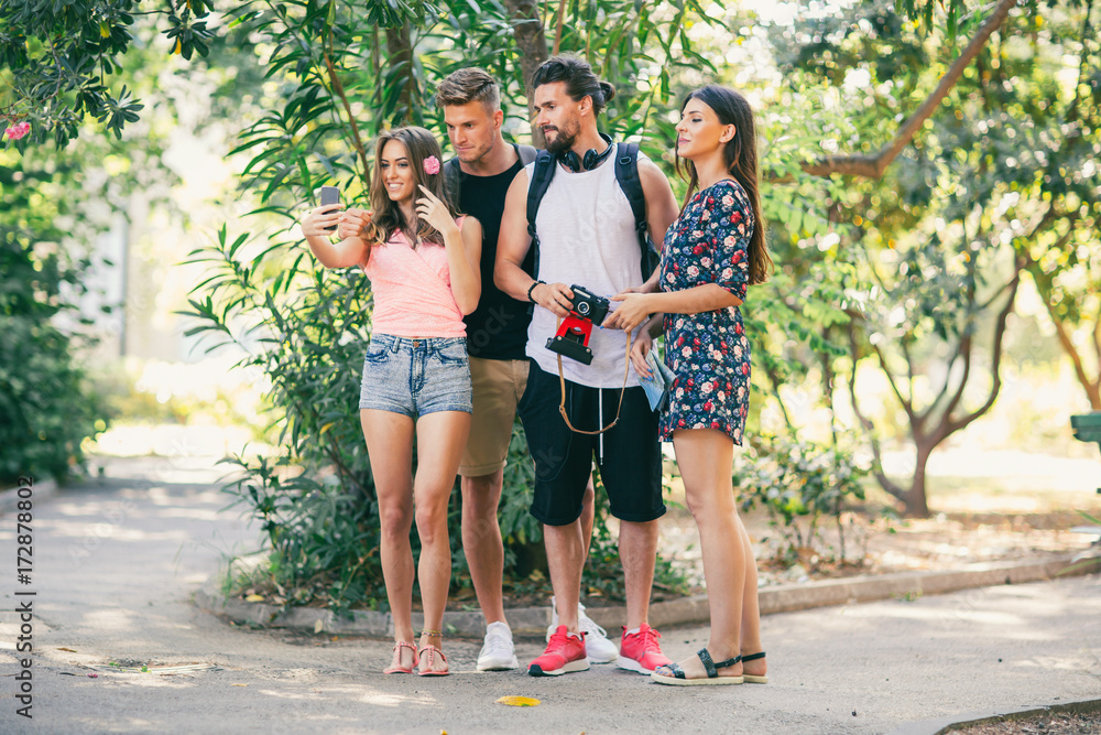 Group of four funny friends taking selfie with a smart phone in summer park Group of four funny friends taking selfie with a smart phone in summer park