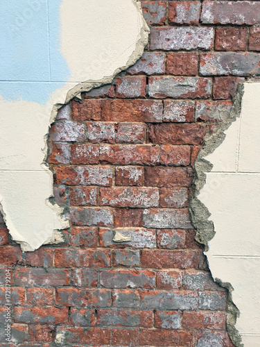 Partially exposed brickwork behind plaster wall of a derelict building.