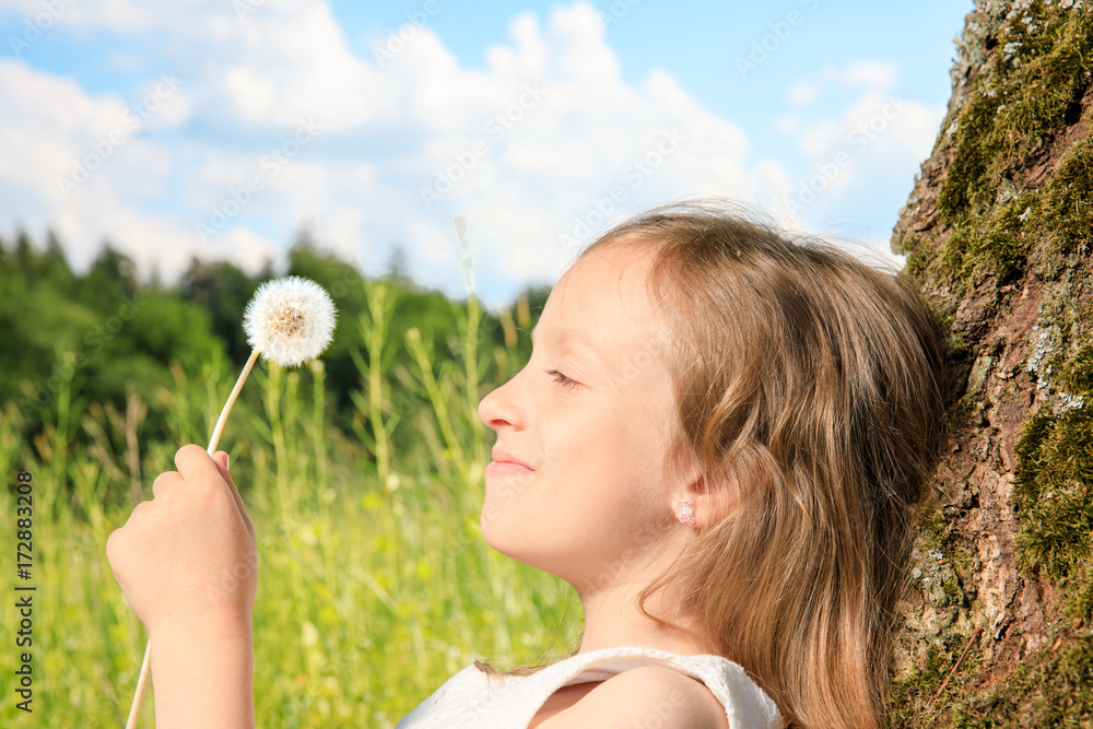 young girl sit next to a tree and smile into the summer sun. she plays with electronic devices, red apple, flowers. sky is blue and the grass is green. young girl sit next to a tree and smile into the summer sun. she plays with electronic devices, red apple, flowers. sky is blue and the grass is green.