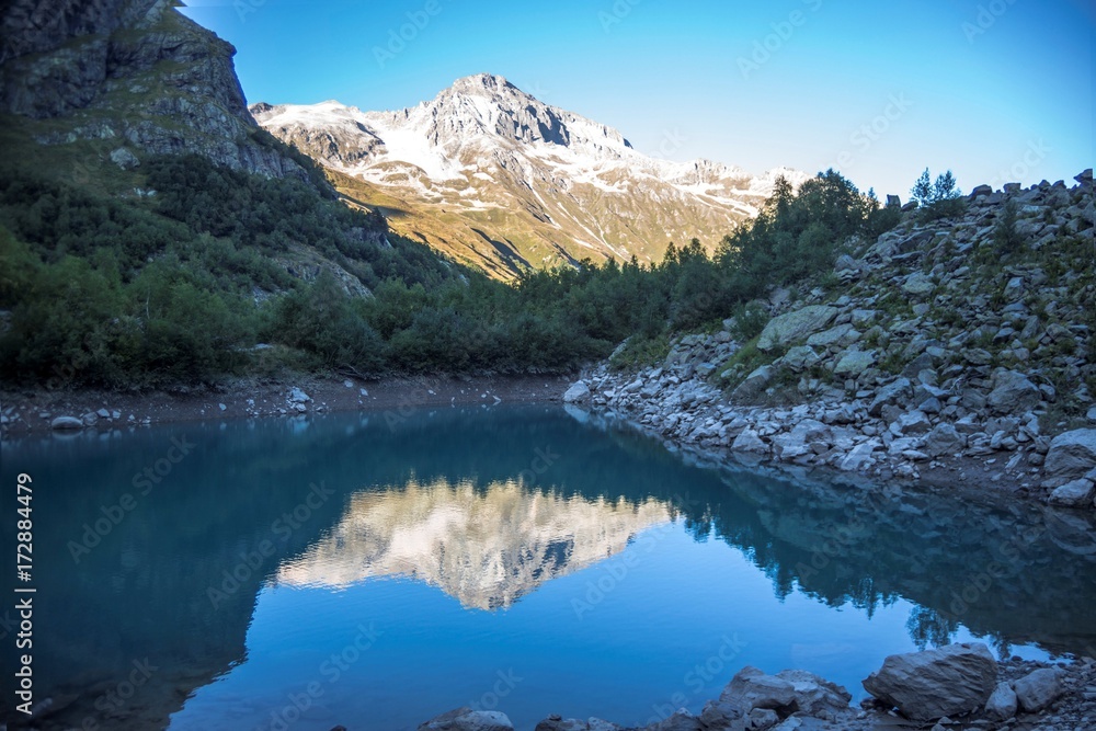 Красивое горное озеро, отражение высоких скал в чистой воде, дикая природа Северного Кавказа, Домбай