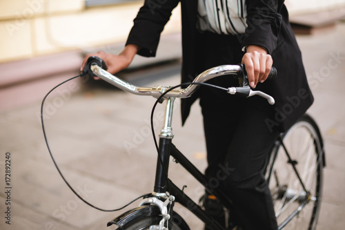 Close up photo of woman body riding on bicycle. Portrait of lady in black suit cycling along the street