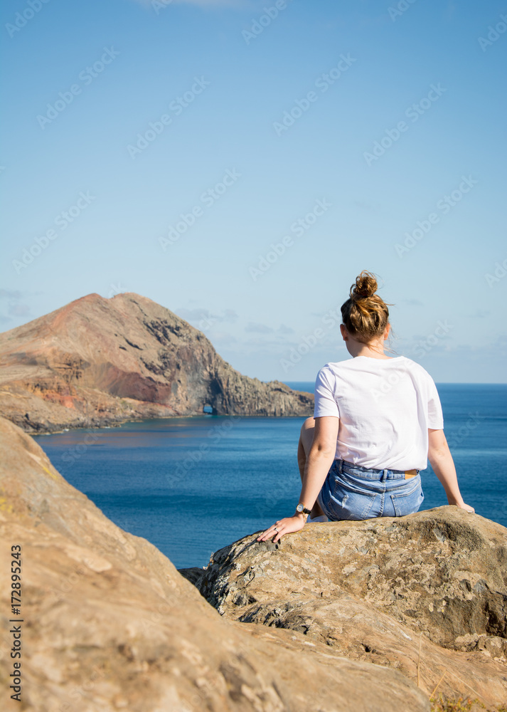 Junge Frau sitzt auf einem Felsen und blickt in Richtung Meer