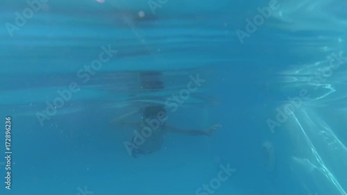 Boy dive in swimming pool and looking at the camera, underwater shoot, sun rays photo