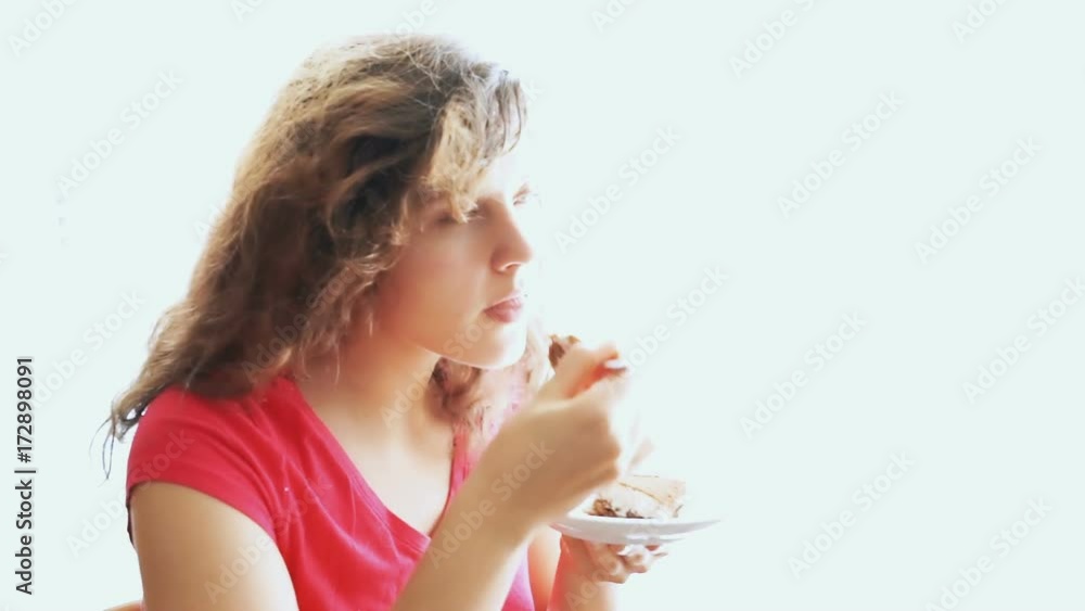 Young woman trying, tasting and eating portion piece of tiramisu cake at kitchen table by bright sunny window from plate in kitchen