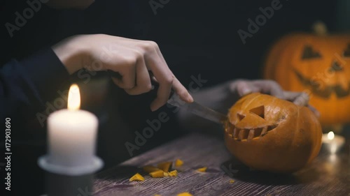 a woman hands cuts out a jack lantern smile with knife and removes seeds from a Halloween pumpkin with a wooden spoon. on a wooden table with kandle. halloween concetp.