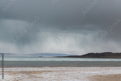 panoramic view of lake with snow on coast and storm clouds in sky 