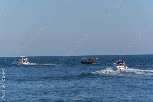Three boats moving through the blue wather. Luxury private motor yacht under way on Black Sea sea with bow wave. People ride in wooden boat.