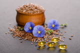 Flax seeds in the wooden bowl, beauty flower and oil in caps on a grey background. Phytotherapy.