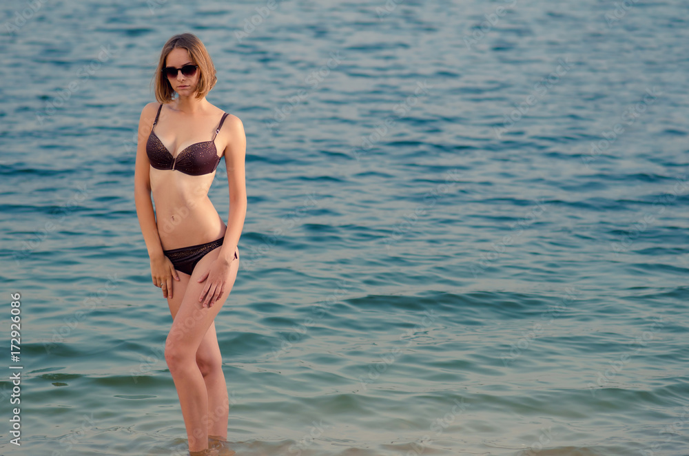 Beautiful caucasian tall young woman with a braun swimsuit in the water on the beach Beautiful caucasian tall young woman with a braun swimsuit in the water on the beach