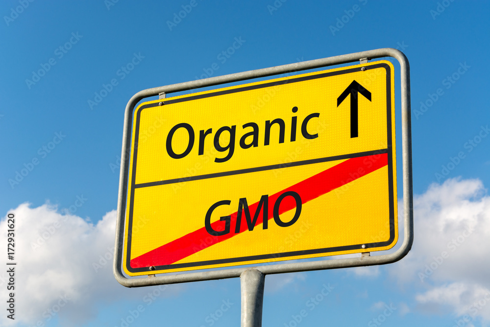 Yellow street sign with Organic ahead leaving GMO behind close up behind