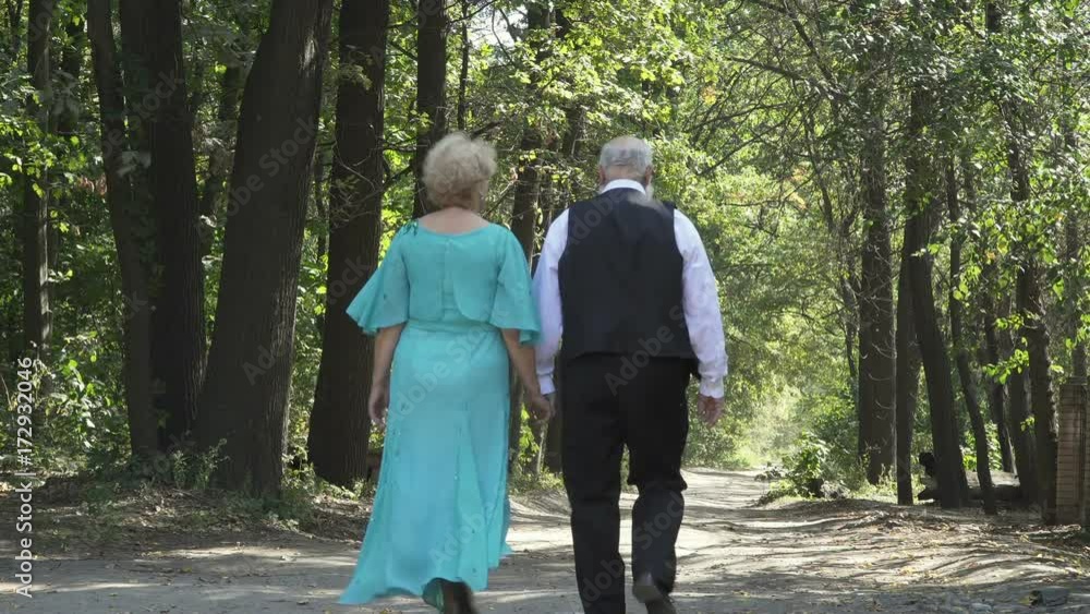 Couple os seniors walks along alley Couple os seniors walks along alley