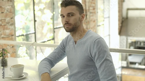 Handsome man in blue sweater sitting in the cafe and showing thumbs up to the camera, steadycam shot
 photo