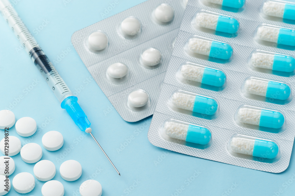 Many capsule medicines, injection syringe and pills on blue background. Various drugs and medicines. Pharmaceutical care.
Many capsule medicines, injection syringe and pills on blue background. Various drugs and medicines. Pharmaceutical care.