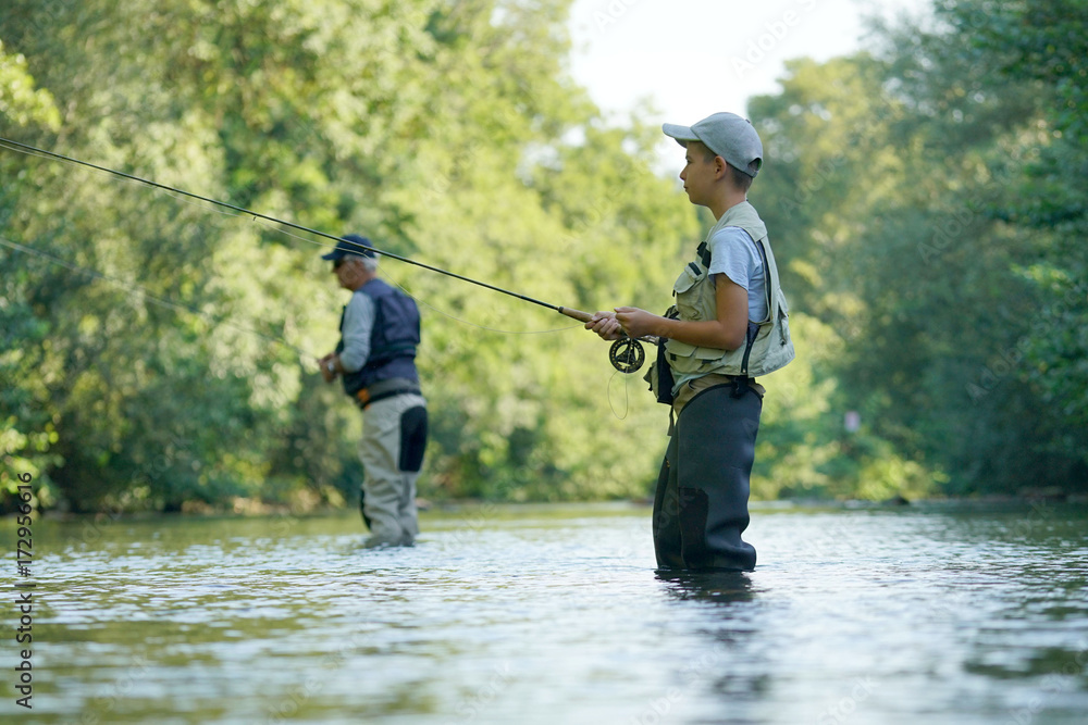 Young boy fly fishing in river, dad in background Young boy fly fishing in river, dad in background