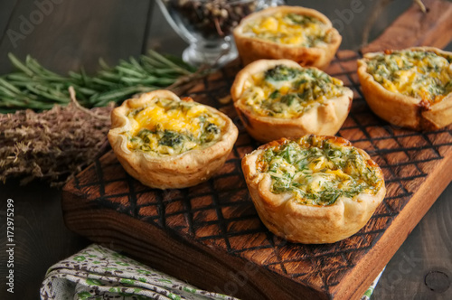 Savory mini quiches (tarts) on a wooden board. Flaky dough pies. Fresh rosemary and dry thyme on a wooden background. photo