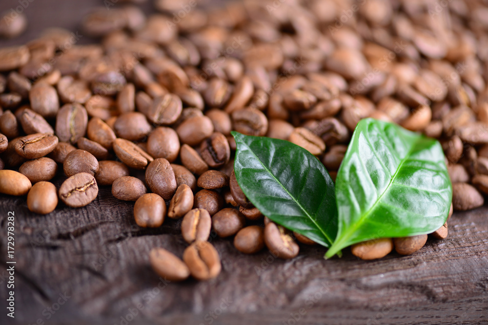 Naklejka premium Coffee beans and green leaves of coffee plant on an old wooden desk. Top view of coffee beans with a copy space for your text. Macro background. Close up.
