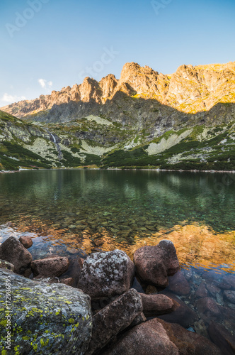 Mountain Lake with Waterfall and Rock in Foreground at Sunset. Velicka Valley, High Tatra, Slovakia.