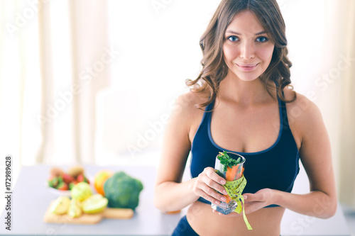 Woman holding a drinking glass full of fresh fruit salad with a tape measure around the glass.