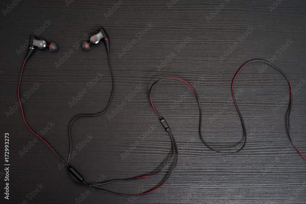 High quality Earphone with Black and Red wire on the black wooden table. High quality Earphone with Black and Red wire on the black wooden table.
