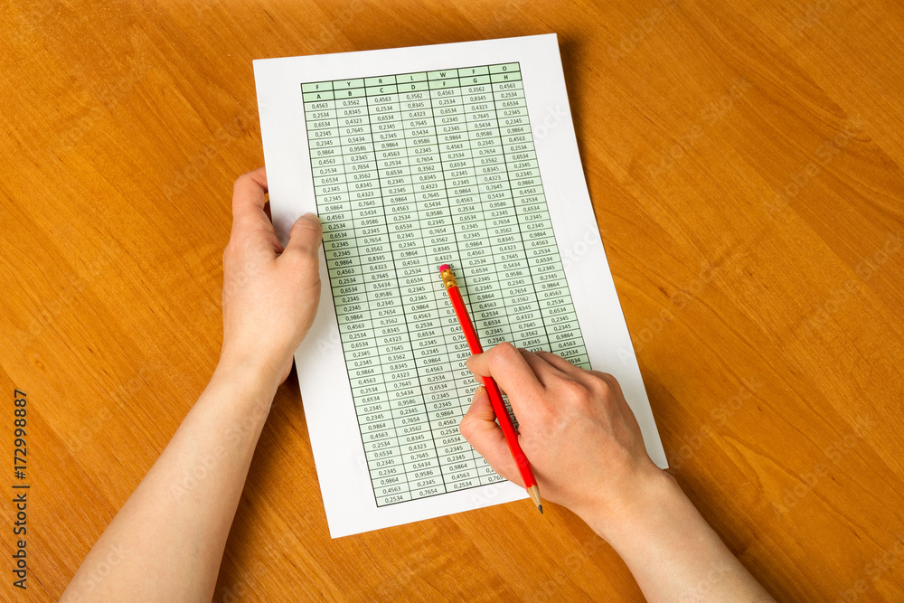Obraz premium Female hands holding pencil and sheet of paper with accounts on the desktop background.
