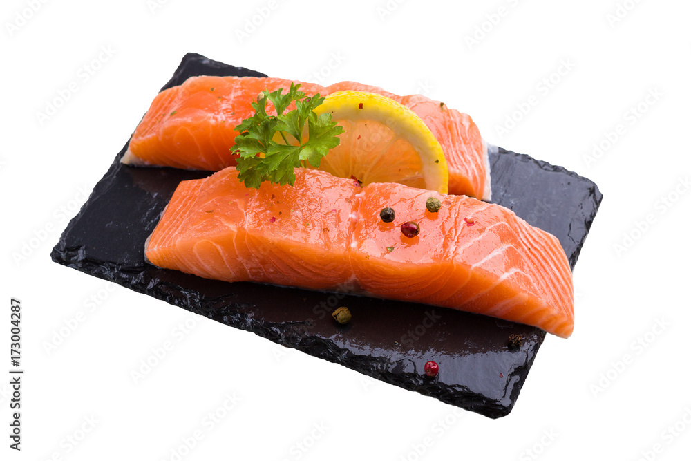 Two pieces of salmon raw fish decorated with lemon slice,parsley leaf and pepper spice, lay on black slate, isolated on white. Two pieces of salmon raw fish decorated with lemon slice,parsley leaf and pepper spice, lay on black slate, isolated on white.