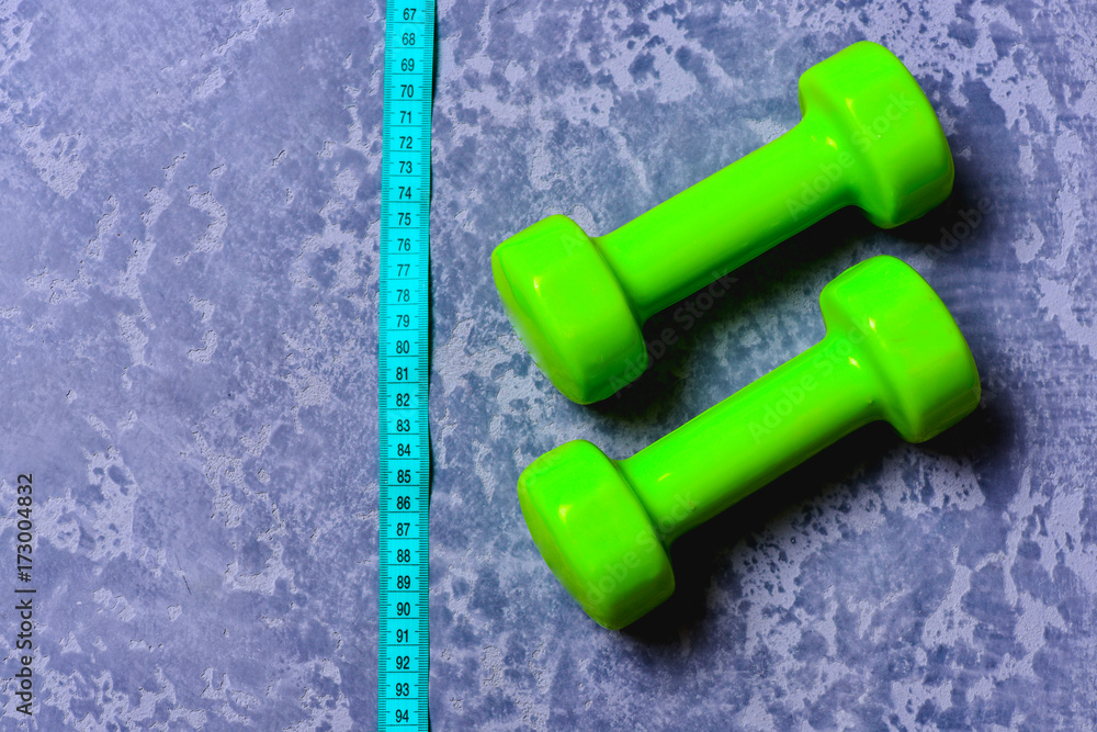 Dumbbells in green color and measuring tape on grey texture Dumbbells in green color and measuring tape on grey texture