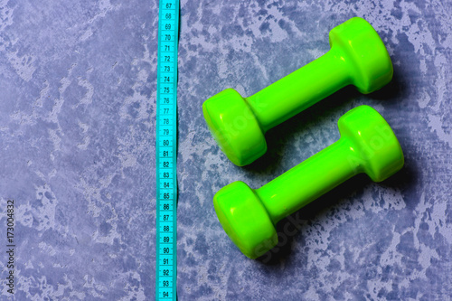 Dumbbells in green color and measuring tape on grey texture