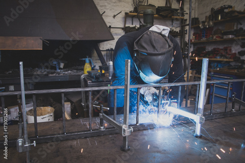 A blacksmith wears safety gear and is welding a metal construction in a metalsmith's workshop.