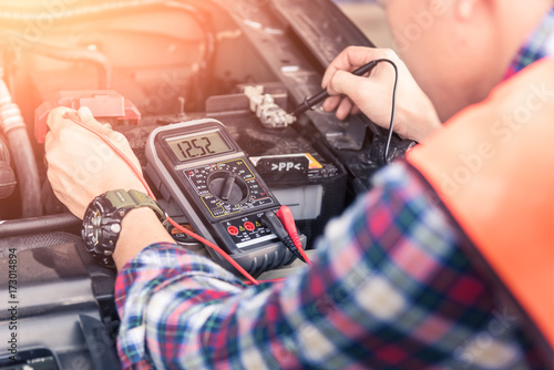 The abstract image of the asian technician using voltage meter for voltage measurement a car battery. the concept of automotive, repairing, mechanical, vehicle and technology.