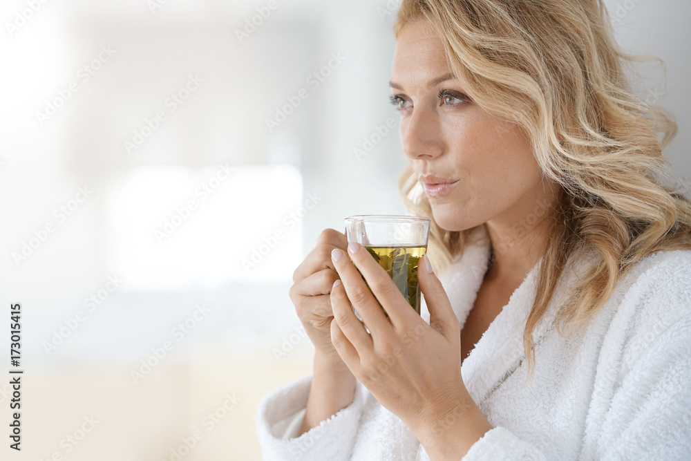Portrait of attractive 40-year-old woman in bathrobe drinking infusion Portrait of attractive 40-year-old woman in bathrobe drinking infusion