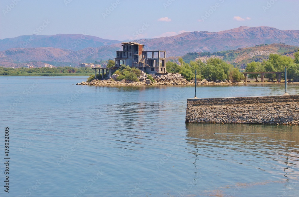 On the banks of Lake Shkodra, North Albania. An unfinished building, in the background a suburb of the city Shkoder and the Albanian alps. Southeast europe.
