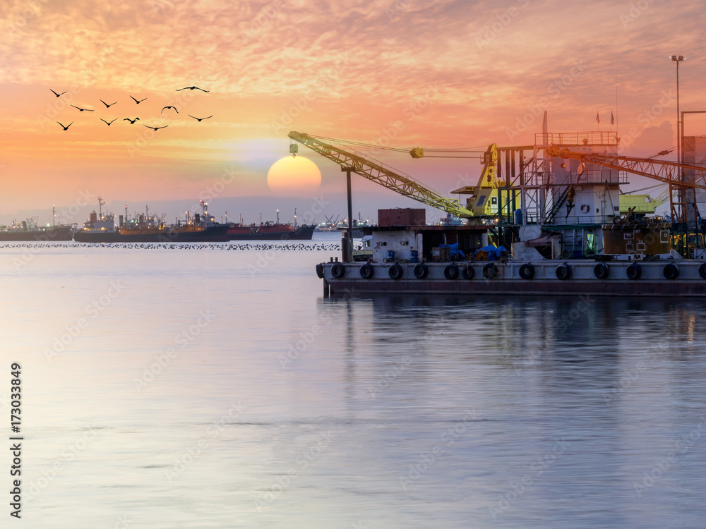 Floating crane moored at industrial port in sunset.