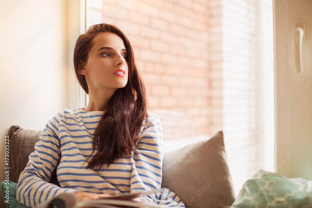 The young beautiful woman lying on sofa in the room and looking in the window The young beautiful woman lying on sofa in the room and looking in the window